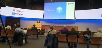 A person standing in front of a podium with a large screen

Description automatically generated